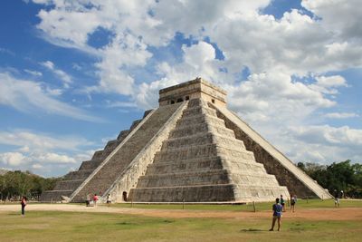 People at kukulkan pyramid of chichen itza against sky