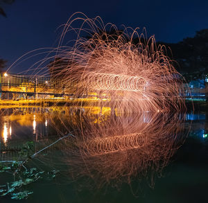 Light trails over river against sky at night