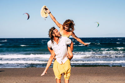 Full length of friends enjoying at beach against sky