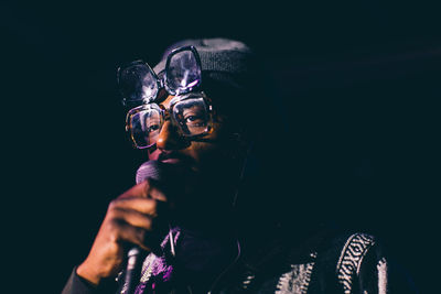 Portrait of young man holding sunglasses against black background