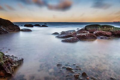 Rocks on shore against sky during sunset