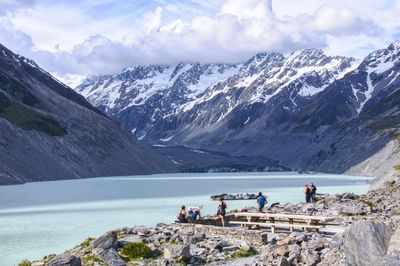 Distant view of people at lakeshore against snowcapped mountains