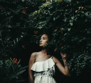 Young woman looking away while standing against plants