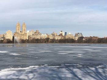 View of frozen river by buildings against sky