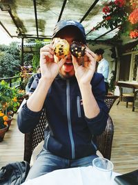 Man holding muffins as eyes while sitting at cafe