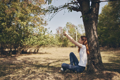 Portrait of young woman sitting on land against trees