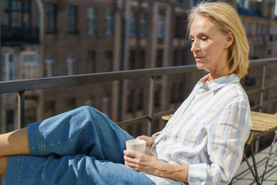 Happy elderly woman sitting on terrace with cup of coffee and enjoying beautiful sunny morning