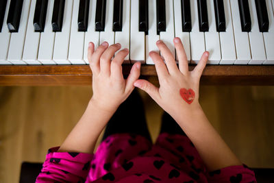 High angle view of childs hands playing the piano with heart tattoo 