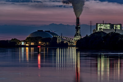 Illuminated buildings by river against sky at night