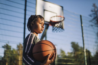 Contemplative girl looking away with basketball on sunny day