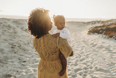 Side view of young toddler girl with mother’s pregnant belly at sunset