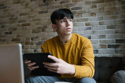 Man using mobile phone while sitting on sofa against wall