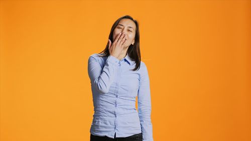 Young woman standing against yellow background