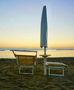 Chair on beach against sky during sunset