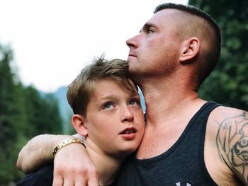 Father embracing son against sky