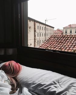 Woman with dyed hair sleeping on bed by window at home