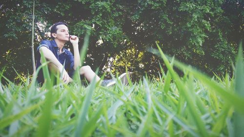 Surface level shot of thoughtful man looking away while sitting on grass