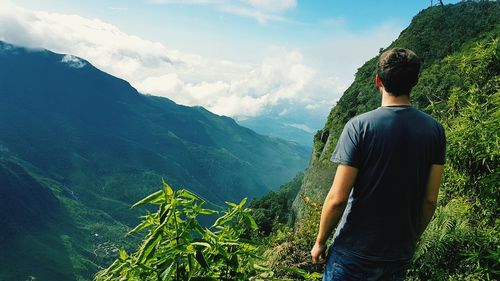 Rear view of man looking at mountains against cloudy sky