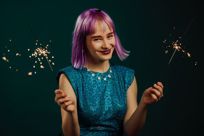 Portrait of smiling woman holding sparkler against black background