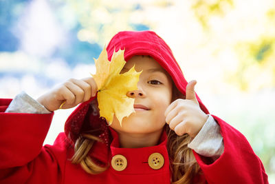 Girl with thumbs up holding leaf during autumn