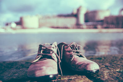 Shoes on riverbank against city