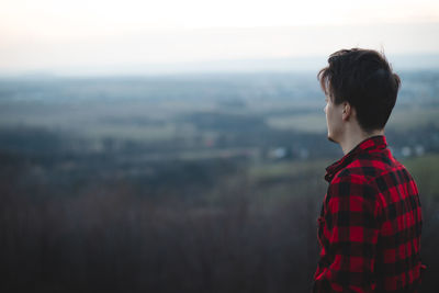 Candid portrait of a man in his 20s dressed in a black and red checked shirt looking into his future