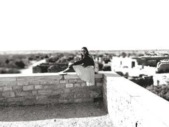 Woman on wall against clear sky