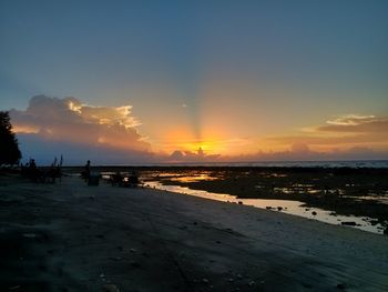 Scenic view of beach against dramatic sky during sunset