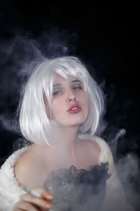 Portrait of female model smoking cigarette against black background