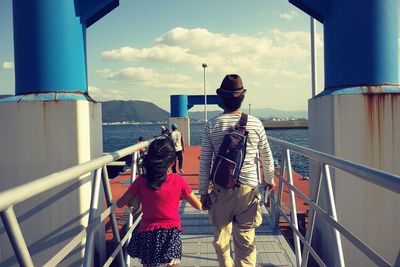 Rear view of father and daughter walking on pier at lake
