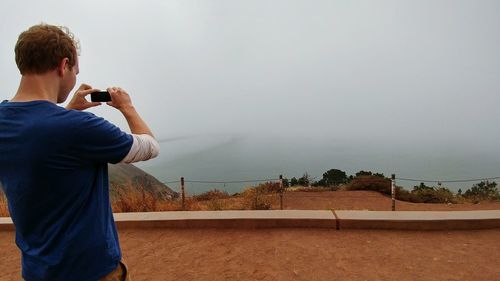 Rear view of man photographing from mobile phone against sky