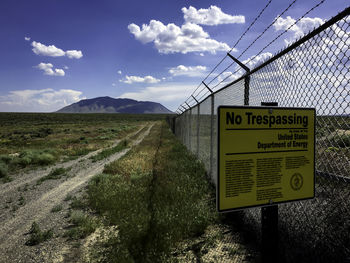 Information sign by fence against sky