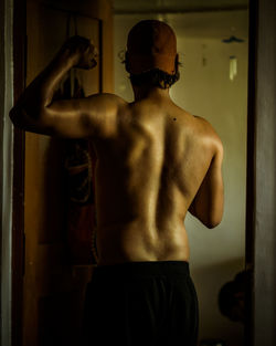 Rear view of shirtless man flexing muscles standing at home