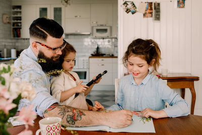 Father assisting girl in homework while sitting with daughter at dining table