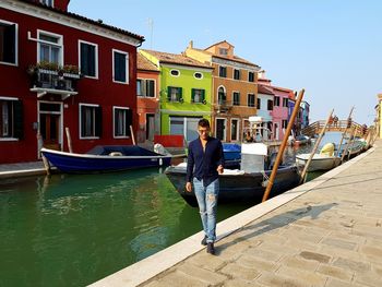 Young man walking against canal and buildings
