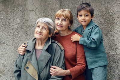 Three generations grandmother great grandmother grandson are standing on the street against a gray 