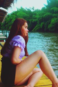 Side view of young woman sitting by lake