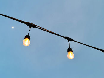 Low angle view of illuminated light bulb against blue sky