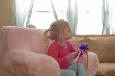 Cute girl with toy sitting on sofa at home