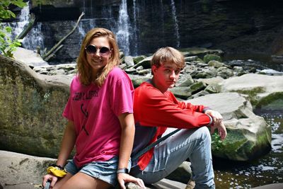 Portrait of couple sitting on rock against waterfall