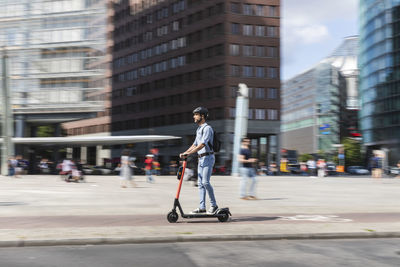 Businessman riding e-scooter on the pavement in the city, berlin, germany