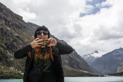 Portrait of woman wearing sunglasses holding mobile phone against mountains