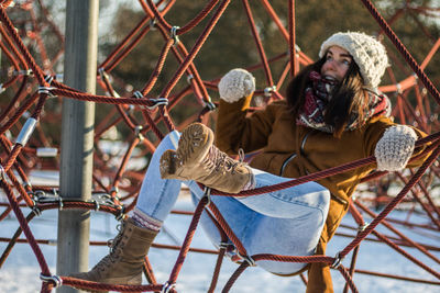 Full length of smiling woman looking up while resting on ropes at snow covered park