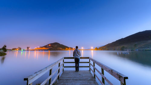 Rear view of man standing on pier at dusk