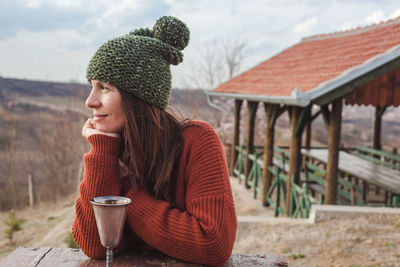 Smiling woman looking away with drink in container on table during winter