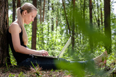 Side view of woman using mobile phone in forest