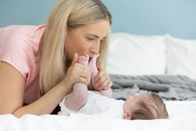 Mother kissing newborn girl legs on bed at home