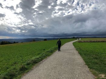 Rear view of person walking on road amidst field against sky