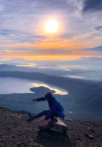 Man balancing on rock at mountain against sky during sunset