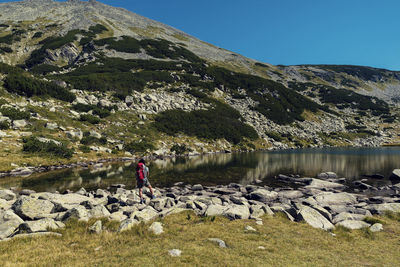 Rear view of man standing on rock by lake against sky